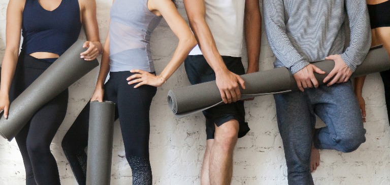 Gruppe Menschen in Sportkleidung mit Yogamatten an der Wand stehend